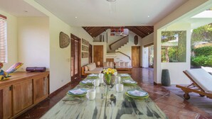 A spacious dining area with a long table set for a meal, a staircase leading to an upper level, and a ceiling fan. - Bali Villa Near the Beach, 2064 (Seminyak)