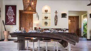 A dining area with a large wooden table set for a meal, surrounded by bar stools. - Bali Villa Near the Beach, 2064 (Seminyak)