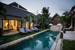 Ein Schwimmbecken mit Liegestühlen, einer überdachten Lounge und einer Steintreppe, die zu einer Terrasse führt.
