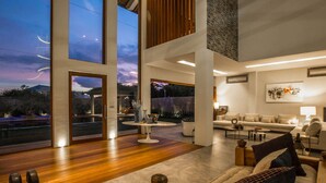 Un vaste espace de vie avec une grande fenêtre donnant sur un jardin, un coin salon confortable avec un canapé et des fauteuils, et un design moderne aux lignes épurées.