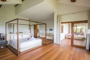 A modern bedroom with a four-poster bed, a sitting area with a sofa, and a view of the outdoors.