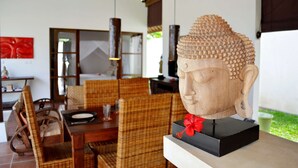 A room with a dining area featuring wicker furniture, a Buddha head sculpture on a pedestal, and a red flower decoration. - Luxury Villa in Bali near Beach, Bali Villa 2031 (Ubud)