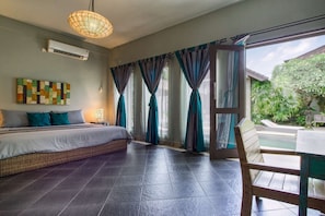 Un dormitorio con cama, cortinas, lámpara colgante y vista a una piscina y follaje exterior.