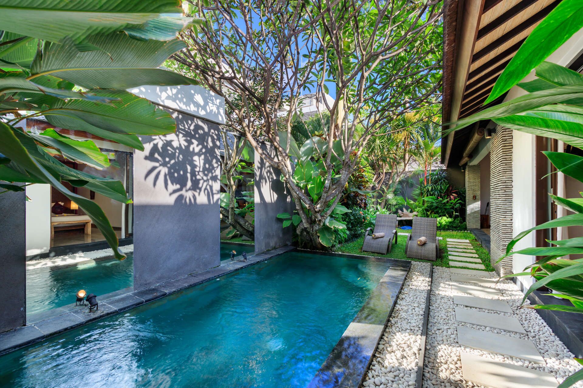 Un espace piscine paisible, avec une piscine à l’eau d’un bleu limpide, entourée d’une végétation luxuriante et agrémenté d’une pergola en bois.