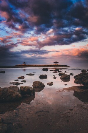 A tranquil beach scene with two gazebos on a small island, surrounded by calm waters and scattered rocks. - Villa for Rent in Bali 2010 (Kerobokan)