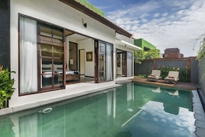 A modern villa with a swimming pool, large sliding glass doors, and a patio area with lounge chairs.