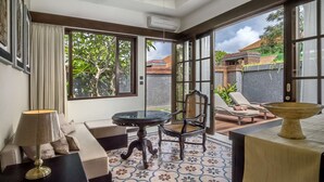 A room with a glass table, a chair, a sofa, and a view of the outside. - Villa for Rent in Bali 2010 (Kerobokan)