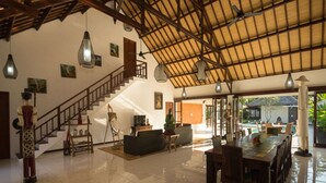 A spacious living area with a high ceiling, a staircase, and a dining area with wooden furniture. - Luxury Villa in Bali near Beach, Bali Villa 2036 (Ubud)