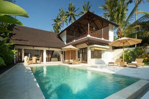 A two-story resort with a swimming pool, lounge chairs, and palm trees.