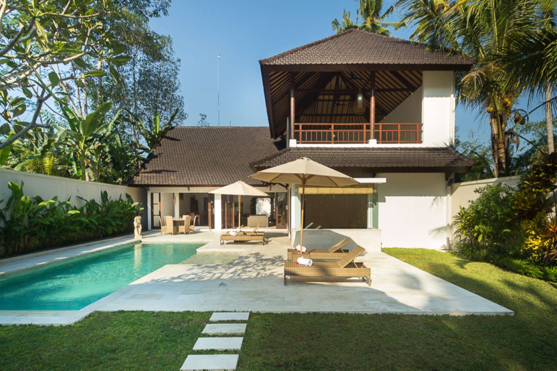 Una casa moderna con piscina, mobiliario exterior y abundante vegetación.