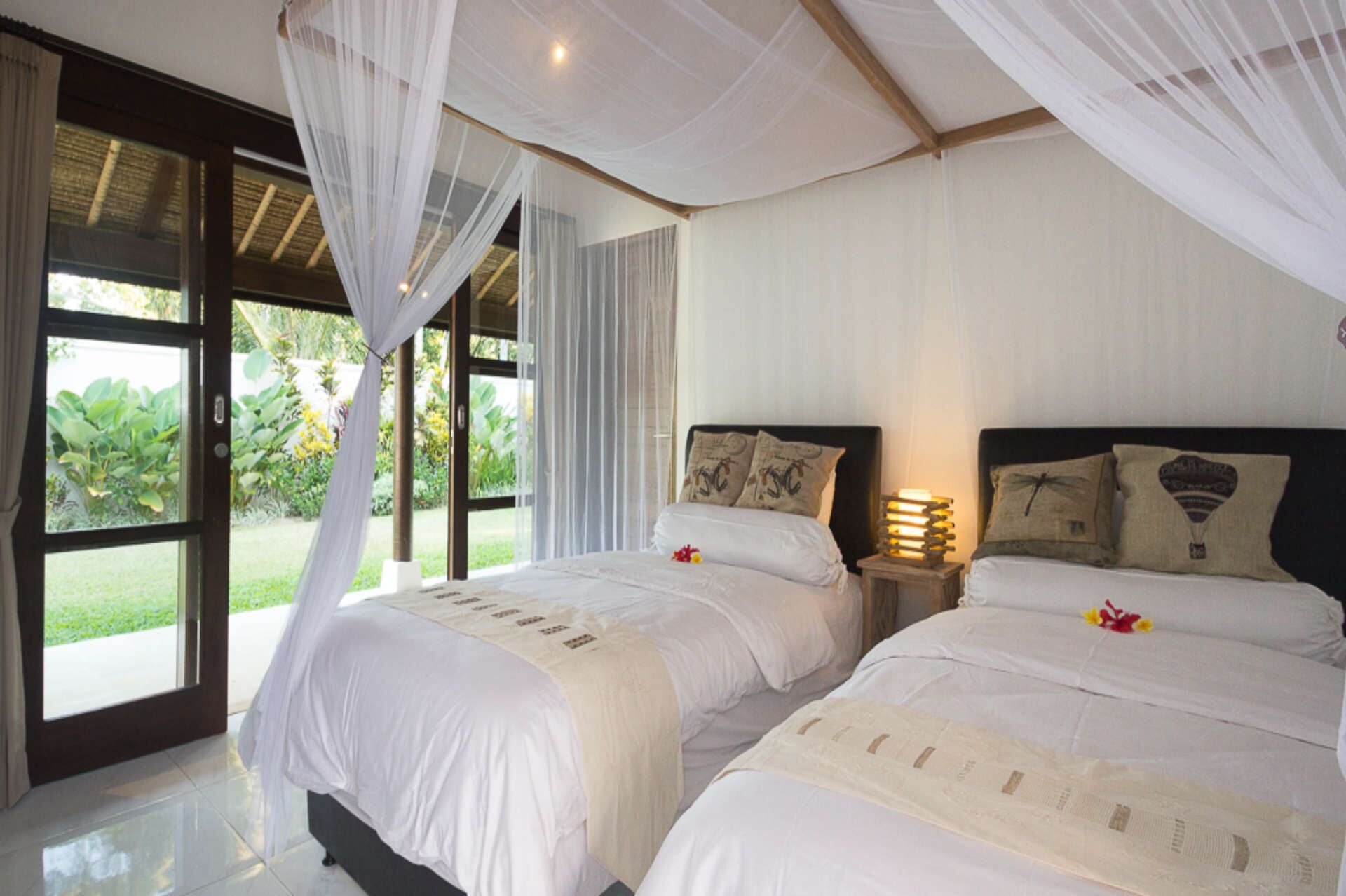 A bedroom with two beds, a canopy, and a view of greenery outside.