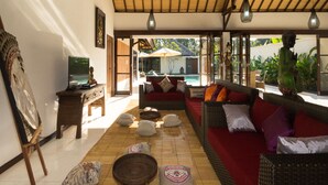A cozy living room with a red sofa, a wooden coffee table, and a large window overlooking a pool.