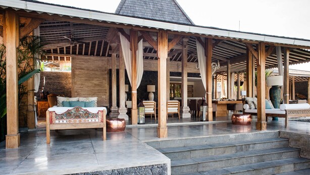 A covered outdoor seating area with a stone wall, wooden furniture, and a staircase leading to an upper level. - Luxury 12 Bedroom Villa With Private Pool, Bali Villa 2027 (Kerobokan)