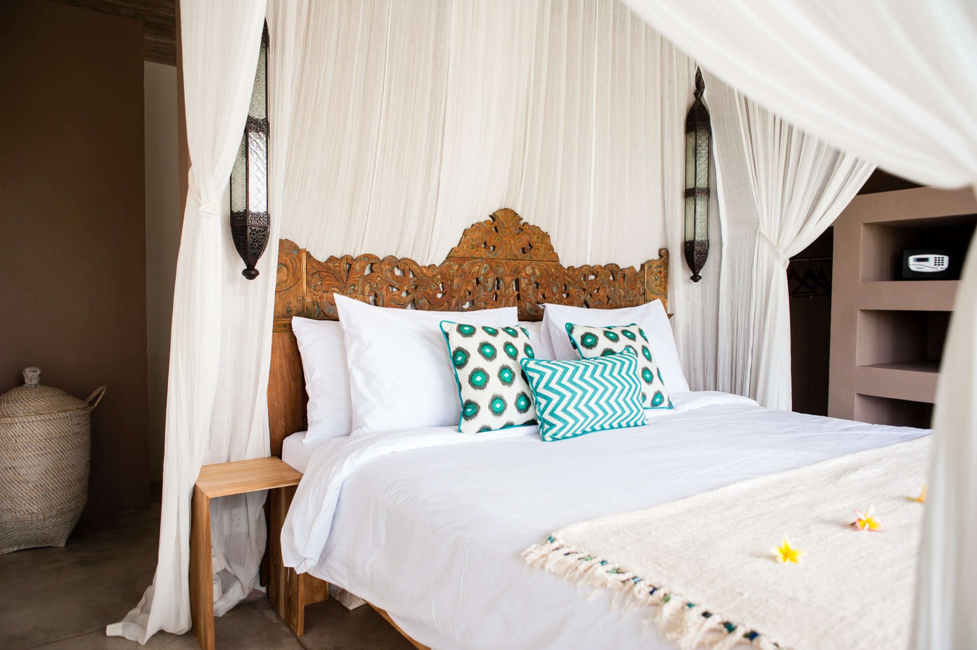 Een bed met een houten hoofdbord, wit beddengoed en decoratieve kussens.