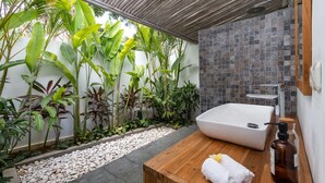 Ein modernes Badezimmer mit einer freistehenden Badewanne, einem Holzwaschtisch und verschiedenen tropischen Pflanzen.