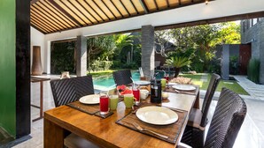 A dining area with a pool view, featuring a wooden table, wicker chairs, and a tropical garden backdrop. - Beautiful Villa With Private Pool, Bali Villa 2026 (Seminyak)