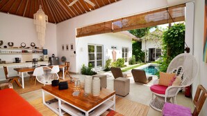 A spacious living area with a wooden coffee table, white wicker chairs, and a view of a pool and garden. - Bali Villa Near the Beach, 2070 (Seminyak)