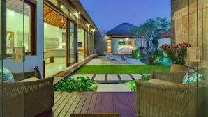 A modern house with a covered patio, a well-maintained lawn, and a visible bedroom with a bed and nightstand. - Imagine Your Family Renting a Luxury Holiday Villa Close to Seminyaks Main Attractions, Villa Bali 2043 (Seminyak)