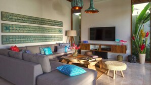A modern living room with a grey sofa, patterned cushions, a wooden coffee table, and a television on a wooden cabinet. - Imagine Your Family Renting a Luxury Holiday Villa Close to Seminyaks Main Attractions, Villa Bali 2043 (Seminyak)