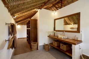 Une salle de bain avec un meuble-lavabo en bois, un grand miroir et un plafond avec des poutres apparentes.