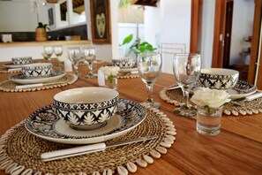 Une table à manger dressée avec des bols, des assiettes et des couverts aux motifs noir et blanc, entourée de sets de table en fibres tressées et d’une rose blanche.