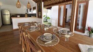 A dining area with a wooden table set for four, surrounded by a kitchen and a view of a garden. - Villa for Rent in Bali 2039 (Seminyak)