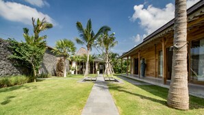 Een tropisch resort met een stenen muur, palmbomen en een houten gebouw met grote ramen.