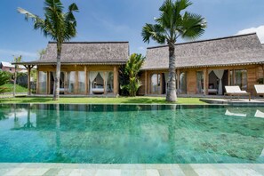 A resort with two wooden buildings, a clear pool, and palm trees. - Villa for Rent in Bali 2008 (Kerobokan)