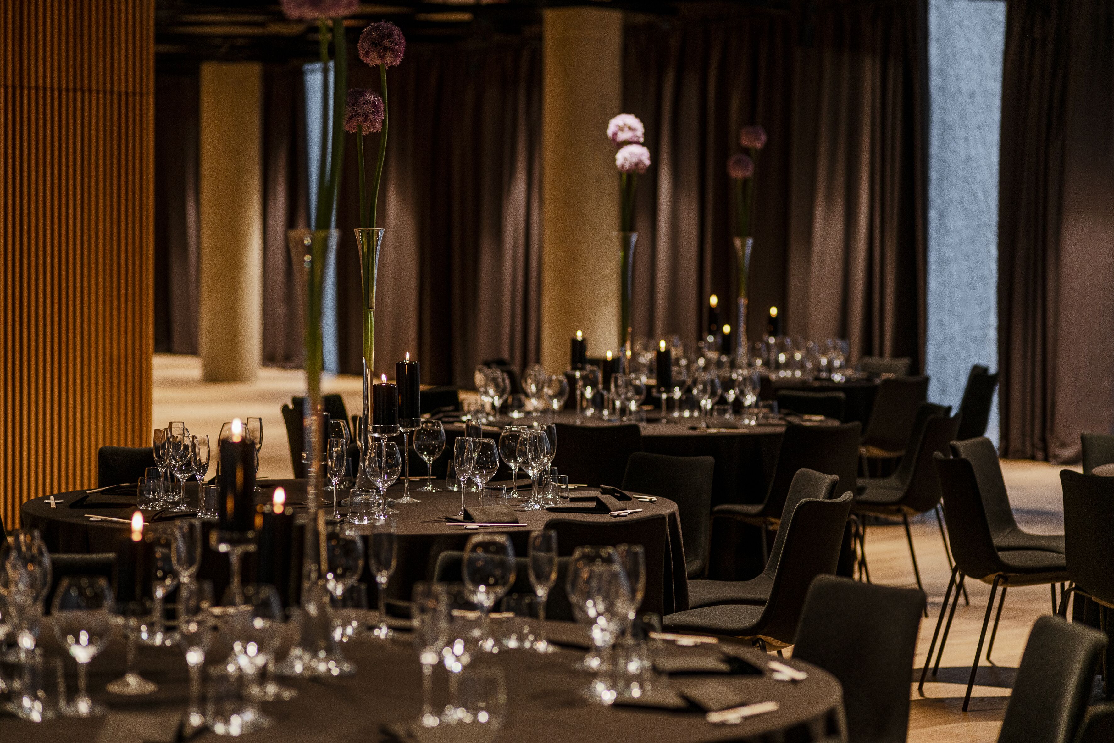 A restaurant with multiple tables set for dining, each with wine glasses, plates, and candles.