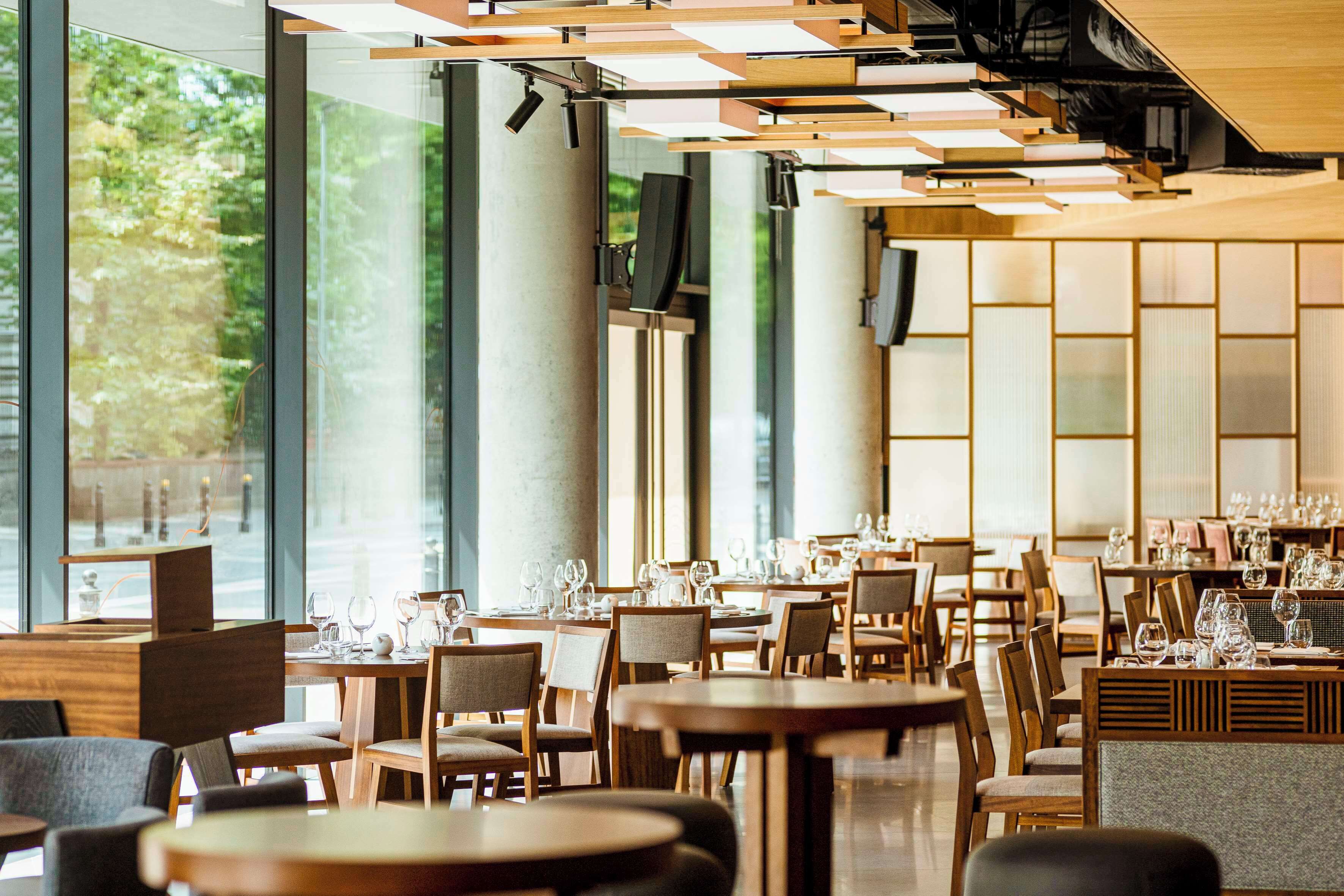 A modern restaurant interior with large windows, wooden tables, and chairs.