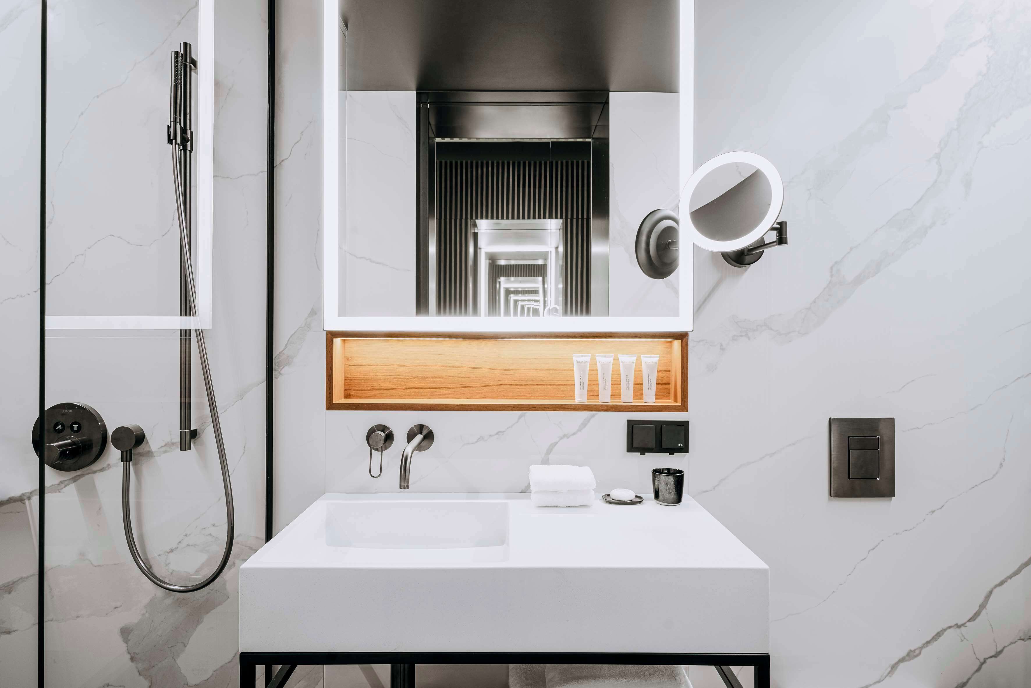 A modern bathroom with a white sink, a mirror with a round frame, and a shower with a handheld hose.