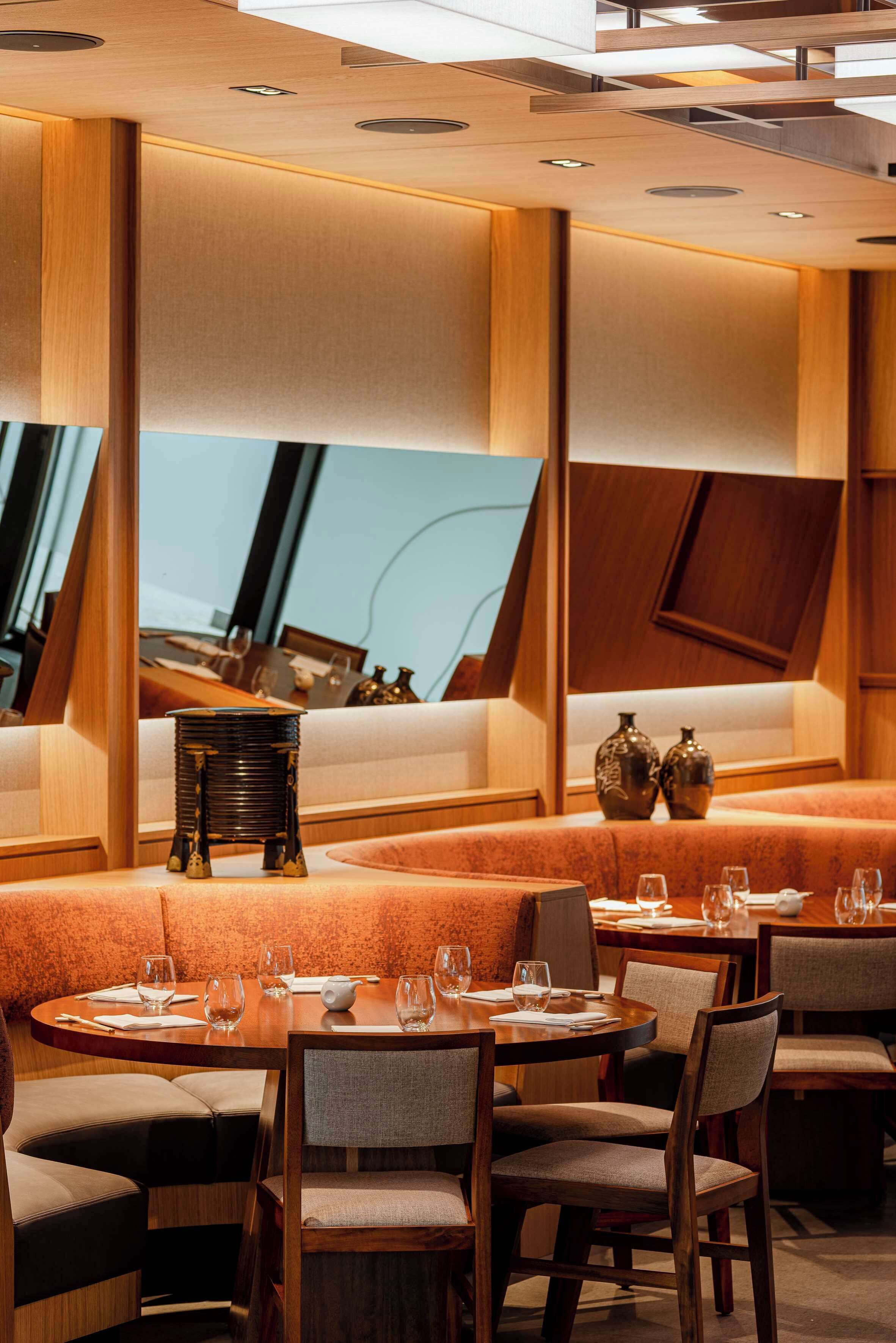 A modern restaurant interior with wooden furniture, round tables, and cushioned seating.
