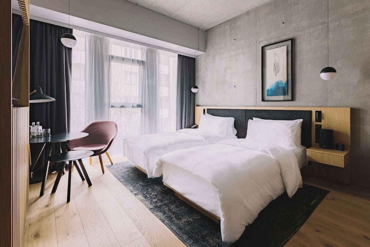 A hotel room with two beds, a desk, a chair, and a large window with curtains.