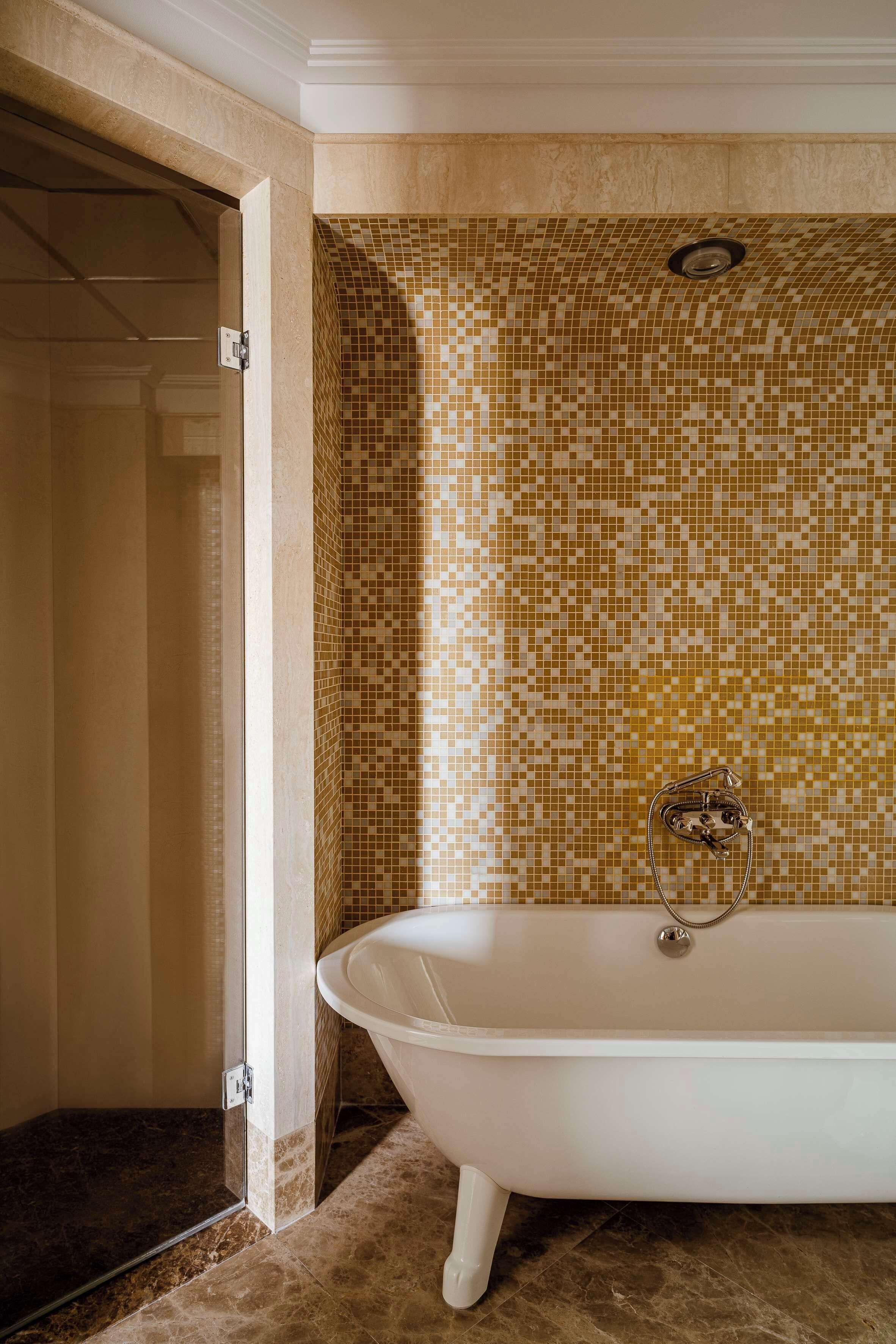 A bathroom with a freestanding bathtub, mosaic tile walls, and a marble floor.