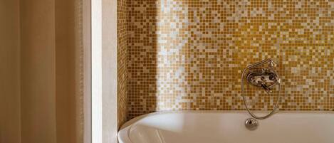 A bathroom with a freestanding bathtub, mosaic tile walls, and a marble floor.