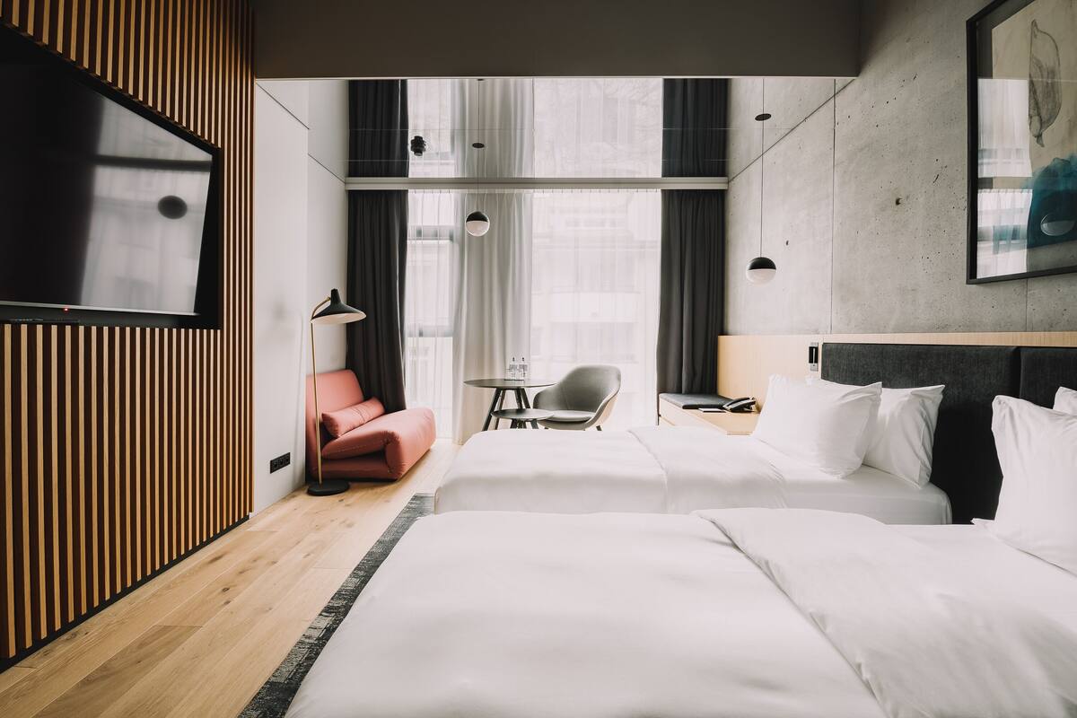 A hotel room with two beds, a TV, a desk with a chair, and a window with curtains.