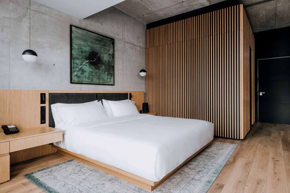 A modern bedroom with a large bed, wooden headboard, and a concrete wall with a green abstract painting.