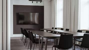 Una sala de conferencias con una mesa larga, sillas negras, un televisor de pantalla plana en la pared y ventanas amplias con cortinas.