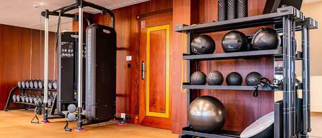 Un gimnasio con equipamiento de levantamiento de pesas, pelotas de ejercicio y mancuernas.