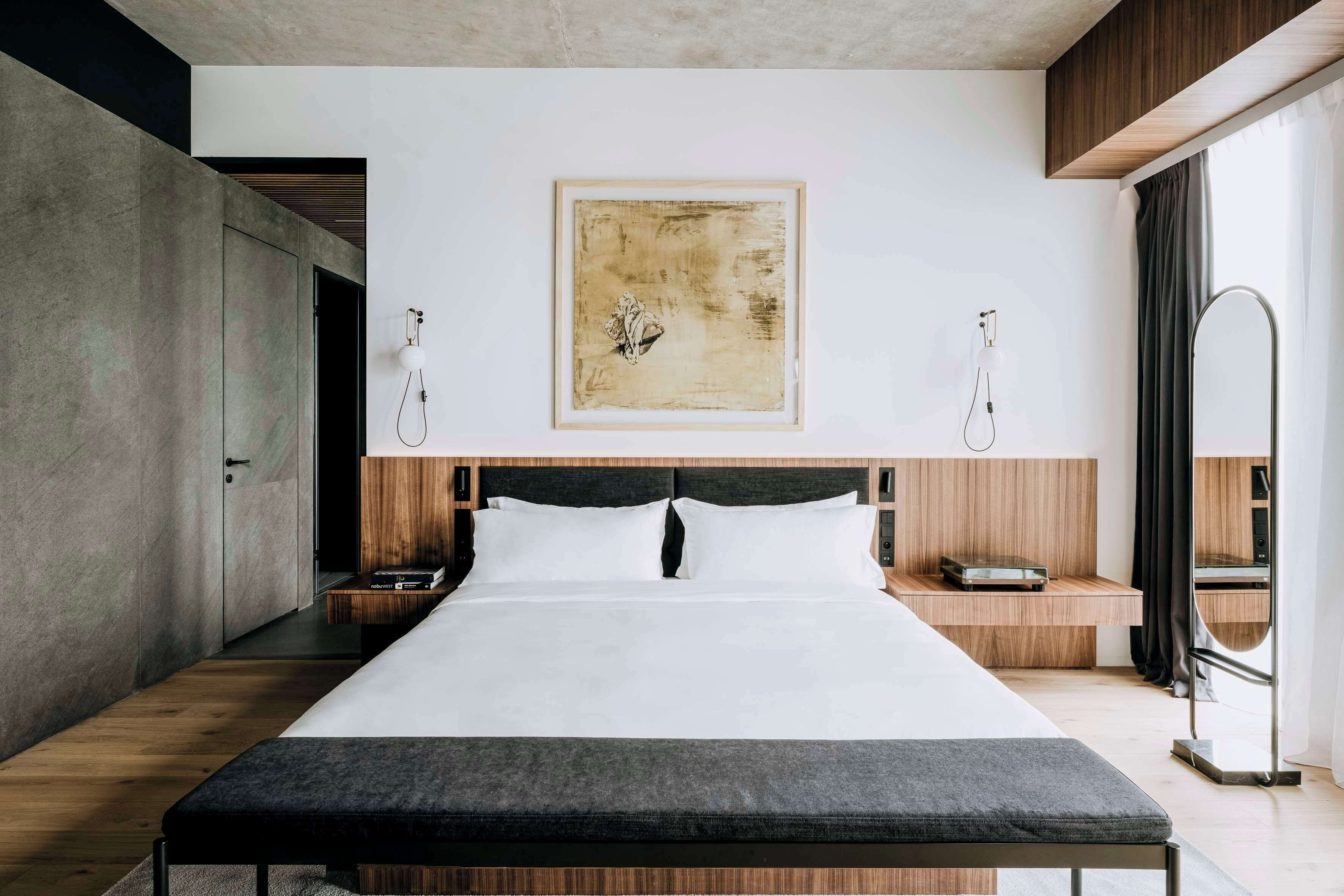 A modern bedroom with a large bed, wooden headboard, bedside tables, and a framed artwork on the wall.