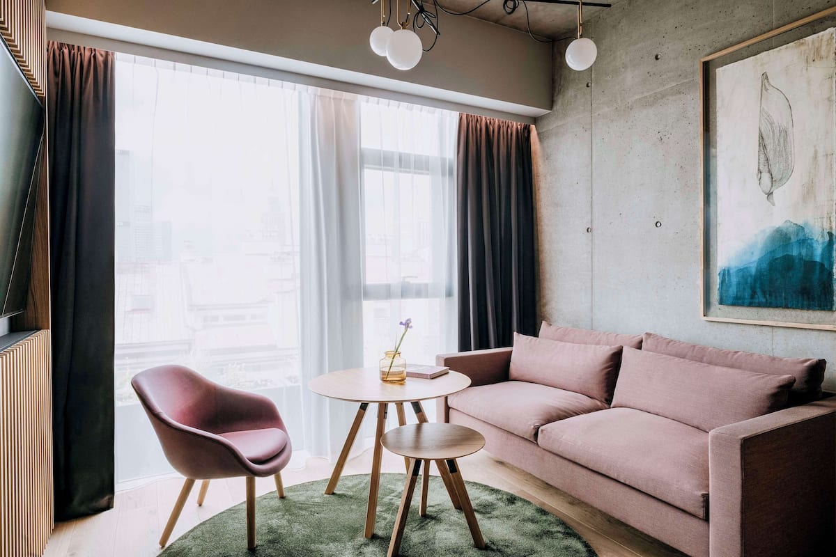 A modern living room with a pink sofa, a round wooden table, and a red chair.