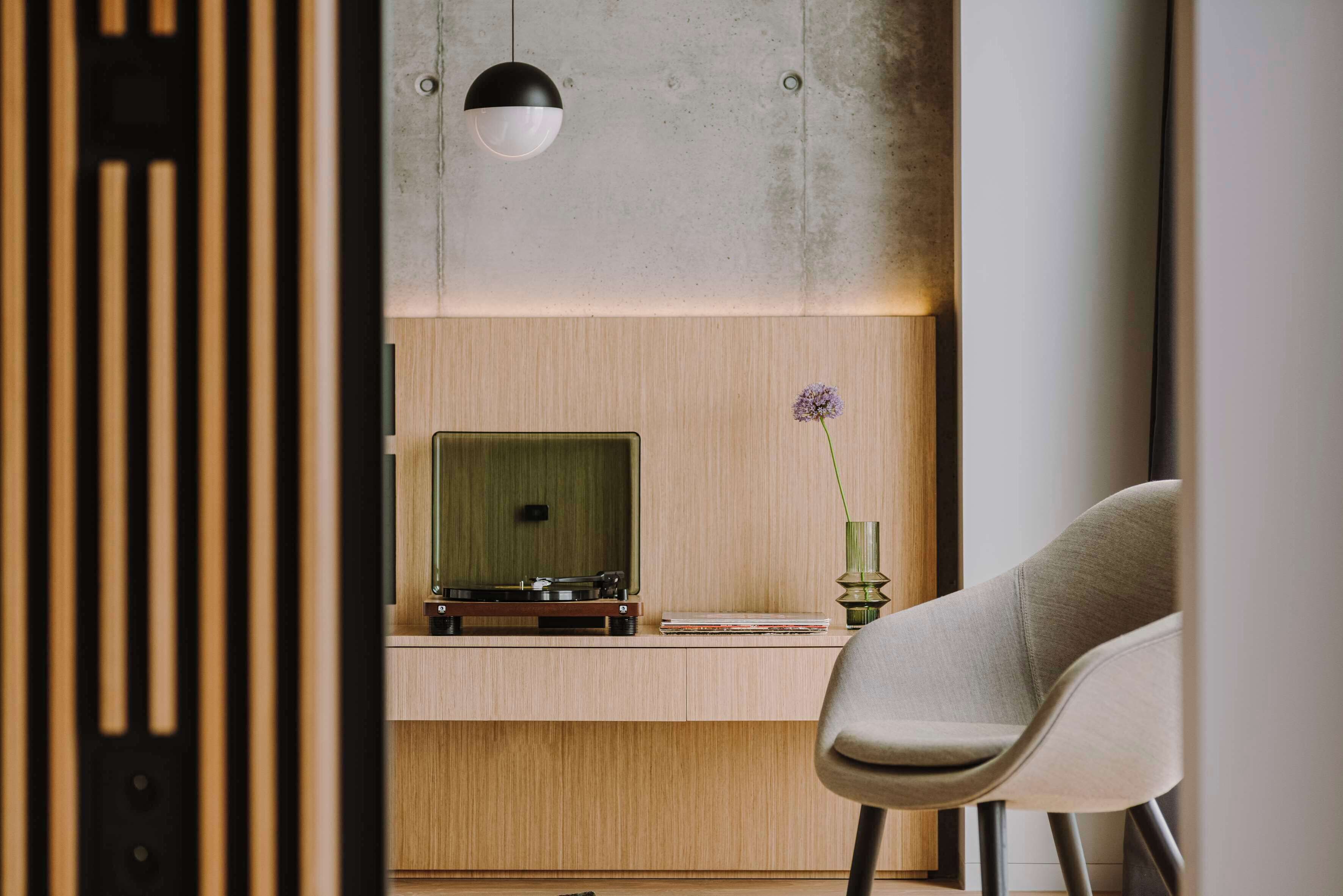 A modern room with a wooden desk, a vintage record player, a green vase with a flower, and a grey chair.