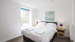 A modern bedroom with a large bed, a window with blue blinds, a bedside table with a lamp, and a wall-mounted artwork. - Sunny Terrace (Maidstone)