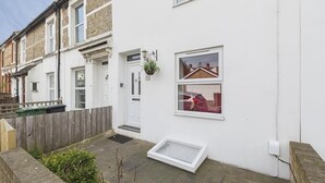 A white townhouse with a small front yard, a white door, and a window with a view of a red car. - Sunny Terrace (Maidstone)