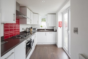 A modern kitchen with white cabinets, a red backsplash, stainless steel appliances, and a window providing natural light.