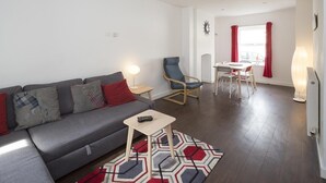 A modern living room with a grey sofa, a small wooden table, and a blue armchair. A dining area with a table and chairs is visible in the background. - Sunny Terrace (Maidstone)