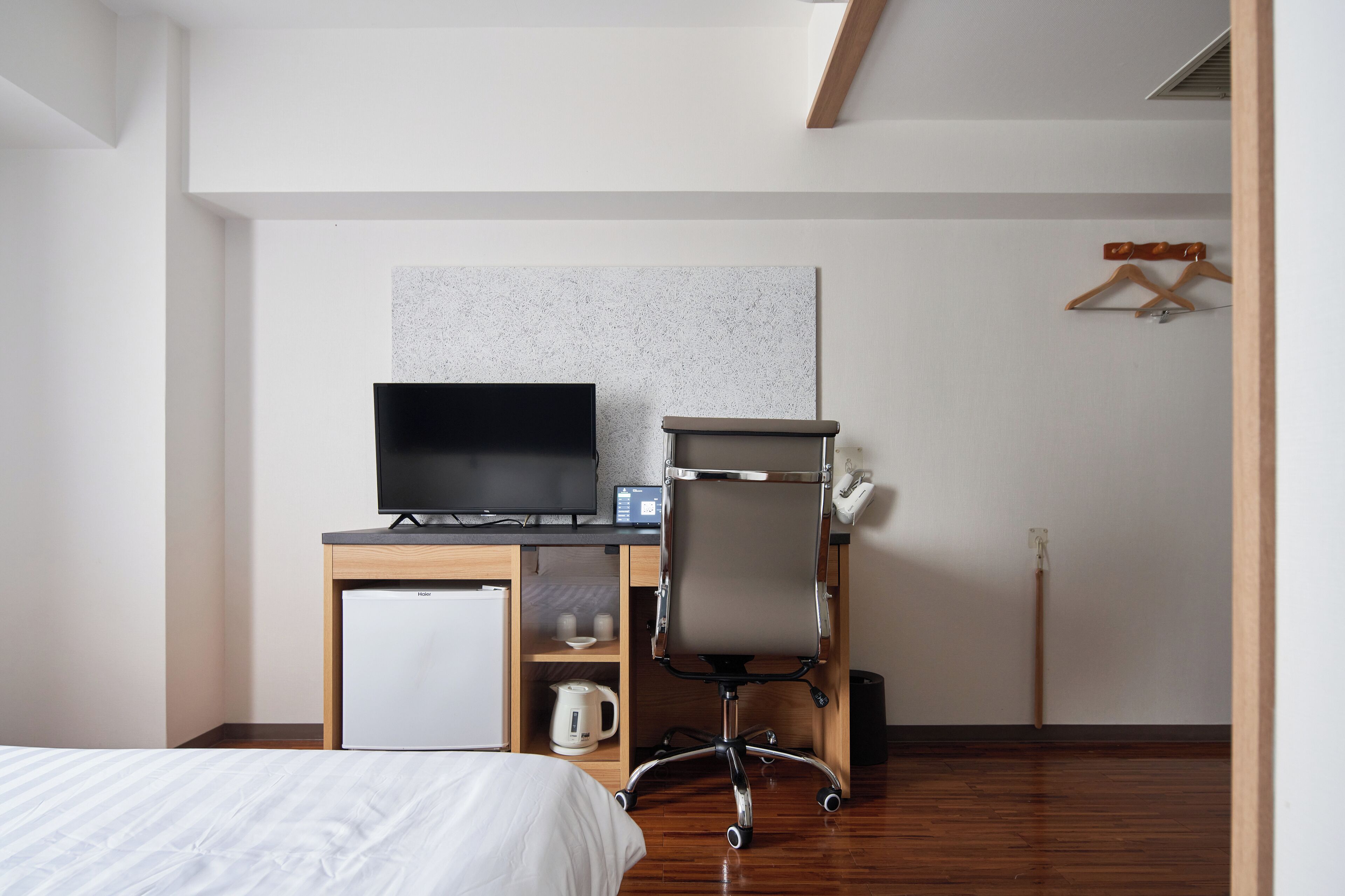 A hotel room with a bed, a desk with a computer, a small refrigerator, and a coffee maker.
