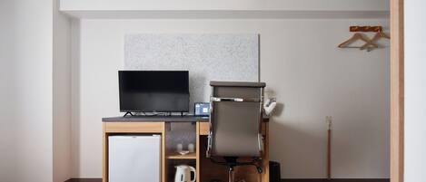 A hotel room with a bed, a desk with a computer, a small refrigerator, and a coffee maker.