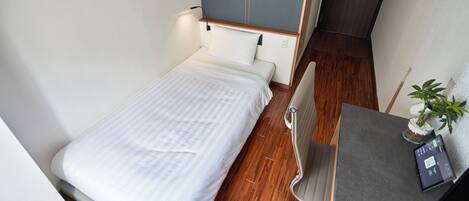 Une petite pièce, bien rangée, avec un lit, un bureau et une chaise.