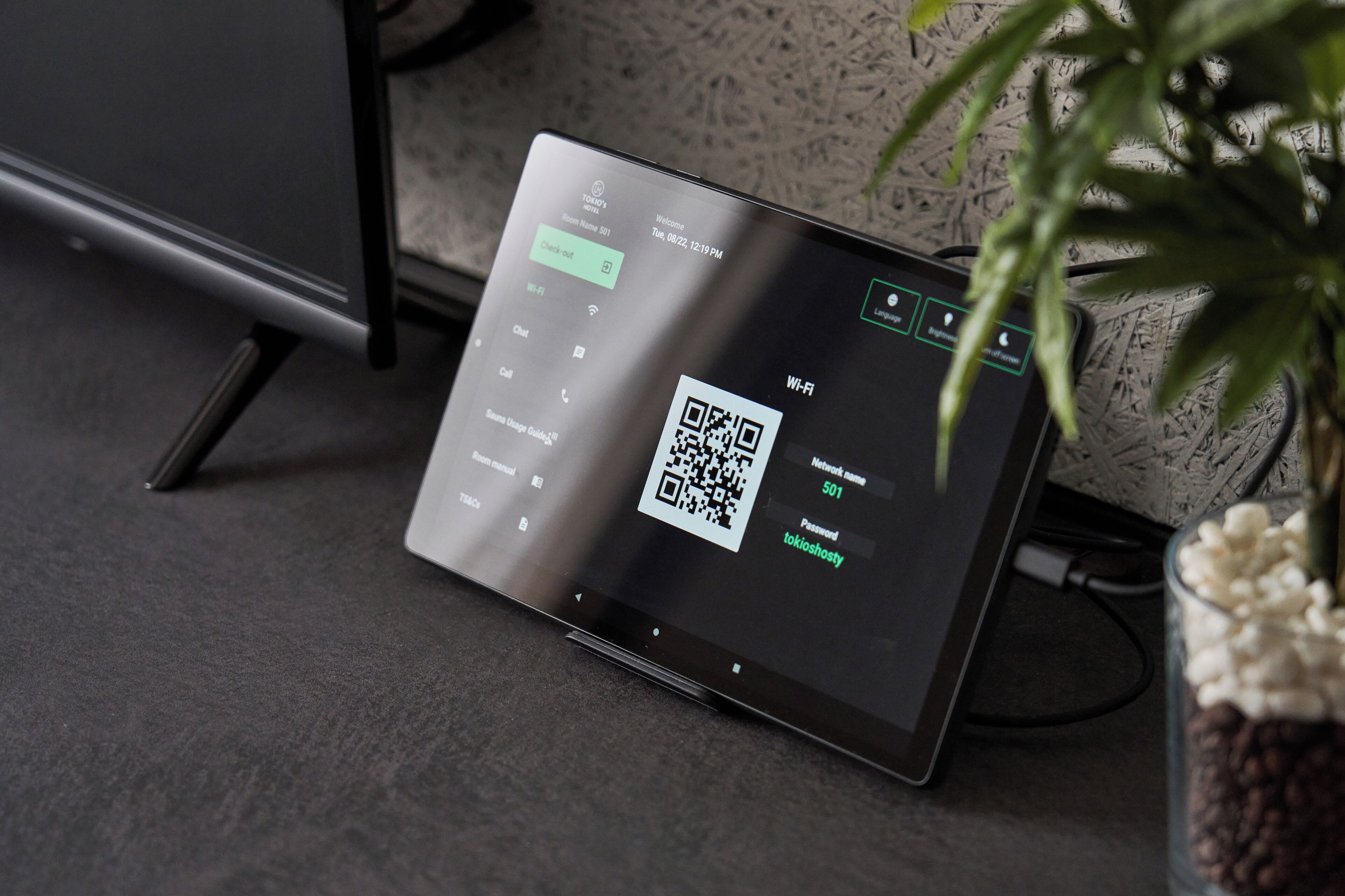 Een tablet toont een QR-code en Wi-Fi instellingen, met een plant en een kabel op de achtergrond.